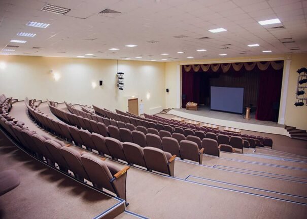Ylhäältä kuvattu auditorio, jossa istuinrivit, puhujakoroke ja valkokangas