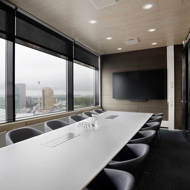 Neuvotteluhuone, jossa pitkä pöytä, suuri näyttö ja videoneuvottelulaitteisto